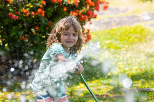 정원에서 꽃 과 식물에 물을 주는아이. 뒷 뜰에 물 호스있는 애. 아이들 정원가꾸기. 아이들은 여름에 집에서 재미있는 야외 활동. — 스톡 사진