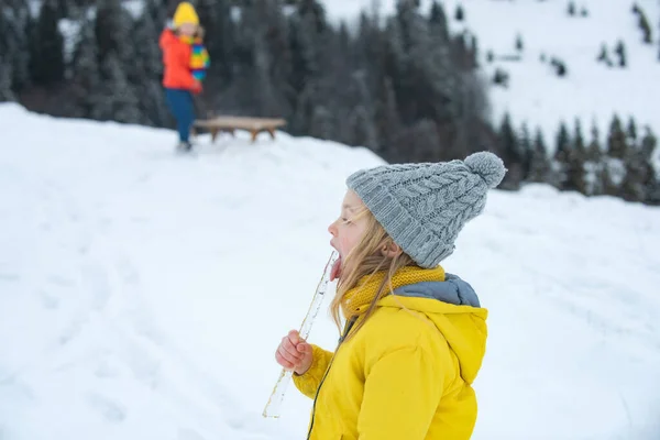 Divertidos niños de Navidad lamen carámbanos de nieve con lengua. Concepto de resfriado y gripe. Niños vistiendo ropa cálida de invierno en clima de nieve. — Foto de Stock