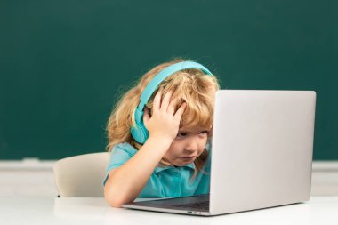 Kızgın üzgün çocuk kulaklık takıyor, sınıfta dizüstü bilgisayarla çalışıyor, müzik dersi dinliyor..