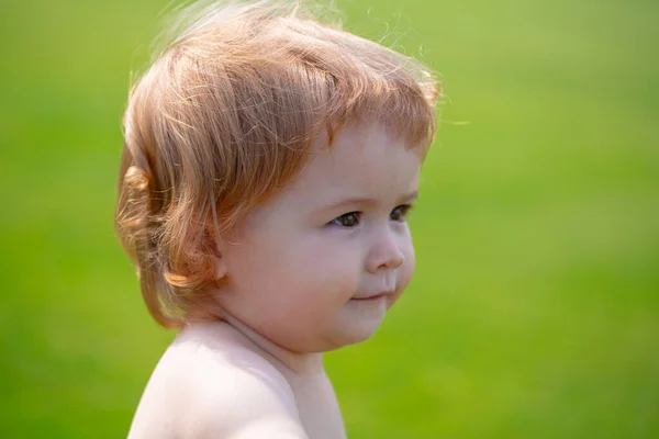 Porträtt av en liten pojke som leker utomhus i gräset. Baby ansikte på nära håll. Lustigt litet barnporträtt. Blond unge, känslomässigt ansikte. — Stockfoto