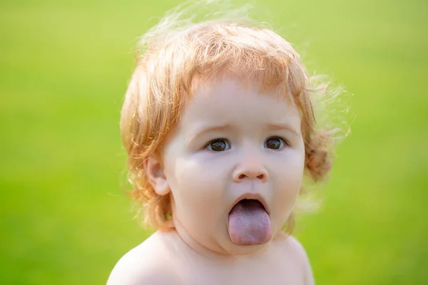 Bébé enfant dans l'herbe sur le fieald en été. Visage de bébé avec la langue fermée. Drôle de petit portrait d'enfant. Enfant blond, visage émotionnel. — Photo