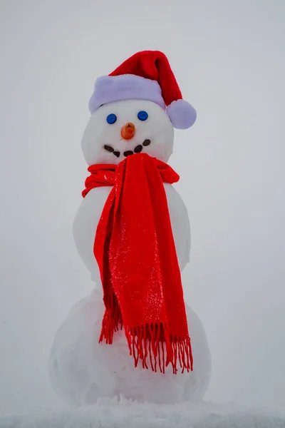 Homem da neve com chapéu de Pai Natal. Boneco de neve engraçado em um prado nevado em um fundo de neve. — Fotografia de Stock