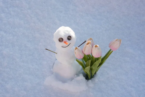 Snö man med våren blommor tulpaner. Rolig snögubbe på snöfältet. Morgonen före jul. — Stockfoto