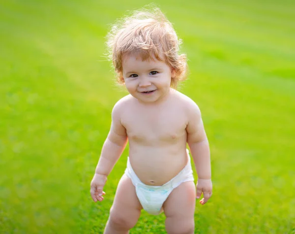 Yeşil çimlerin üzerinde, doğada oynayan, bez takmış küçük bir bebek. Çocuklar oynuyor. Bebek ve yaz güneşli hava. Küçük komik çocuk portresi. Sarışın çocuk, gülen duygu, gülen surat. — Stok fotoğraf