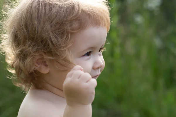 Un niño pequeño juega en el parque. Retrato de un bebé feliz en el campo de hierba. Cara de bebé de cerca. Gracioso retrato de primer plano de niño. Niño rubio, cara de emoción. —  Fotos de Stock