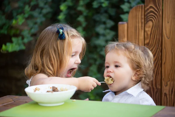 妹が赤ん坊に餌をやる。かわいい面白い赤ちゃんが食べる、赤ちゃんの食べ物、健康的な子供の朝食。食欲あり. — ストック写真