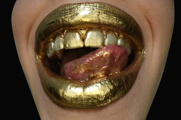 Gold paint on lips. Golden lips, sensual woman mouth. Metallic creative art make up close up. Gold concept. Sexy tongue. Sensual lick.