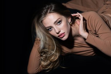 Stüdyoda poz veren genç bir kadın. Siyah stüdyoda şehvetli baştan çıkarıcı pozlar veren seksi bir kız. Yüzünde siyah ışık olan güzel bir kadının moda portresi..