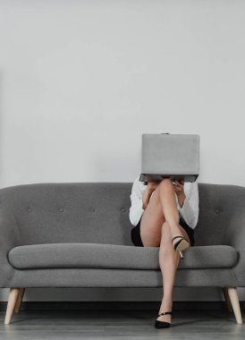 Güzel sekreter bacakları. Seksi bacaklı seksi bir iş kadını. Baştan çıkarıcı kadın yüzünü dizüstü bilgisayarla kapatıyor. Şehvetli sekreter koltukta oturuyor..