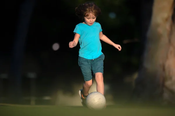 Dziecko bawiące się w piłkę na placu zabaw w parku. Chłopak futbolista kopie piłkę nożną na boisku. Aktywne dzieci. Piłka nożna dla dzieci. — Zdjęcie stockowe