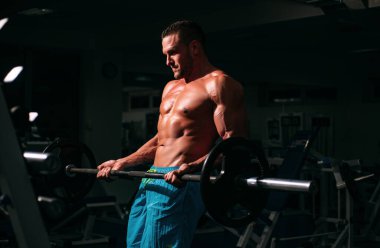 Spor adamı halter kaldırarak biceps yapıyor. Çıplak gövdeli genç kaslı adam spor salonunda çalışıyor. Spor yapan atletik erkek sporcu. Spor konsepti.