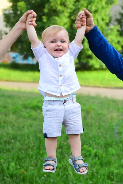 Vader en moeder ouders houden baby handen vast. Lifestyle portret baby kind in happines aan de buitenkant in de wei. — Stockfoto