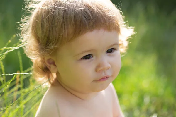 Petit bébé jouant dans la nature sur l'herbe verte. Les enfants jouent. Visage de bébé près. Drôle de petit portrait d'enfant. Enfant blond, visage ému. Bébé et été ensoleillé. — Photo