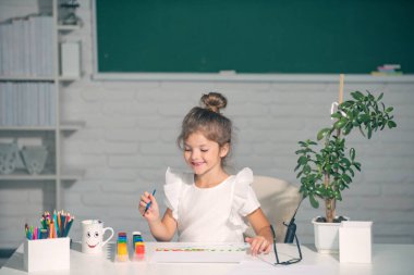 Okuldaki çocuk boyalarla resim çiziyor. Çocukların yaratıcılığı. Komik çocuk suratı.