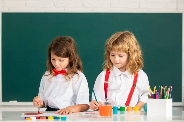 Skolbarn flicka och pojke målning med färger färg och pensel i klassrummet. Syskonteckning med penna och färg. — Stockfoto