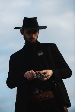 Siyah takım elbiseli ve kovboy şapkalı bir kovboy. Vahşi batı silahları, eski tabanca tabancası ve federal mühimmatı olan ciddi bir adam. Amerikan batı şerifi. Vahşi batı konsepti.