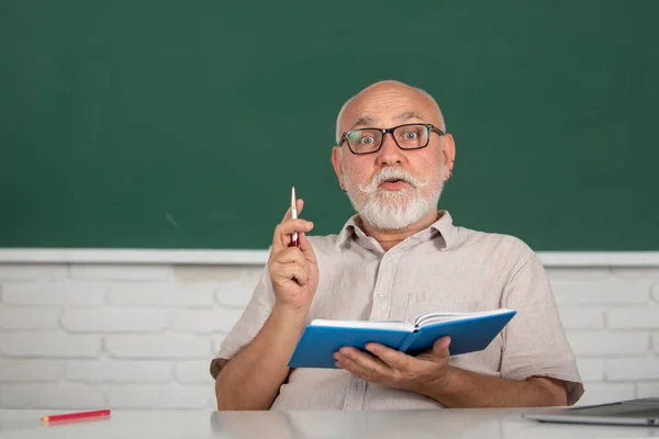 Senior teacher in classroom at university or college. Male old tutor on board with notebook. Lesson seminar skills. Mature man study in high school. — 图库照片