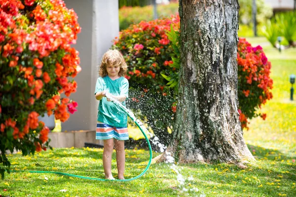 Çocuk bahçede oynuyor, hortumdan dökülüyor, yağmur yağıyor. Mutlu çocukluk kavramı.