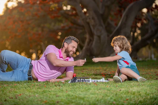 Syn ležel na trávě a hrál šachy s otcem. Inteligentní dítě, chytré děti. — Stock fotografie