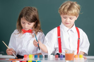 Sınıfta karatahta arka planda komik öğrenciler çiziyor. Okul arkadaşları çocuklar erkek ve kız birlikte resim yapıyorlar..