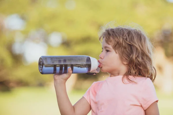 緑の公園のスポーツボトルから可愛い男の子が水を飲む。アウトドアを行使スポーティーな子供のクローズアップ肖像画. — ストック写真