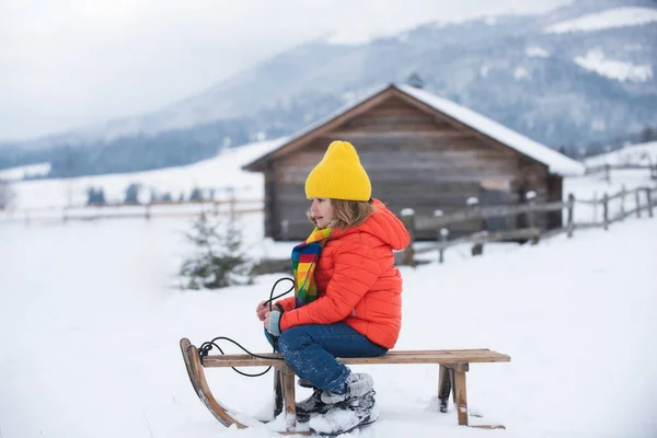 Zimní pletené dětské oblečení. Chlapec sáňkaří v zasněženém lese. — Stock fotografie