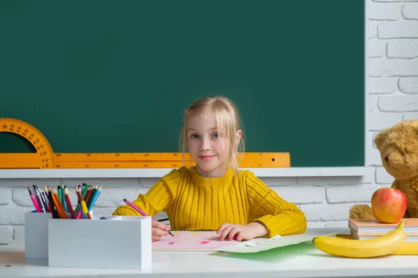 Vissza a suliba. Aranyos diáklány rajzol az asztalnál. Gyerek az osztályteremben táblával a háttérben. Oktatás, tanulás és gyermekkoncepció. — Stock Fotó