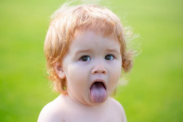 Criança engraçada no parque. Cara de bebê com língua de perto. Engraçado pequeno retrato closeup criança. Menina loira, cara de emoção. — Fotografia de Stock