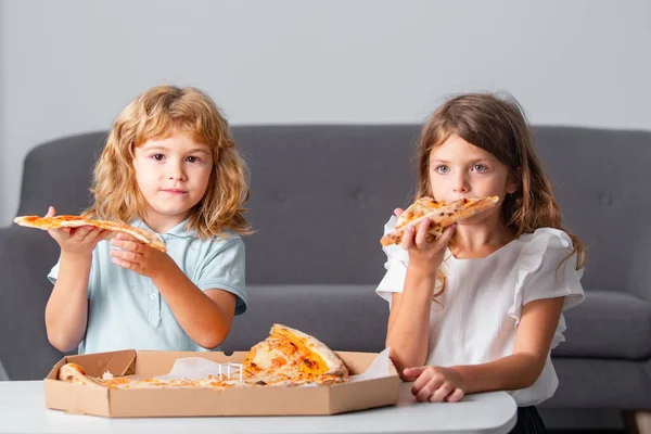 Hija feliz e hijo comiendo pizza. Los niños disfrutan y se divierten con el almuerzo juntos en casa. Pequeños amigos, chico y chica muerden pizza. — Foto de Stock