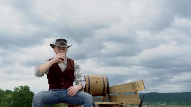 農家やカウボーイの肖像画は、屋外でウイスキーを飲む。アメリカのカウボーイ。ハンサムな残忍な西側の男. — ストック動画
