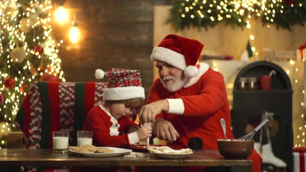 Mikołaj i dziecko w kapeluszu Santa dekorowanie Christmas ciasteczka piernika w kuchni retro w domu. Gotowanie tradycyjnych świątecznych słodyczy. Strona główna piekarnia, jedzenie, choinka i szczęśliwy noworoczne koncepcji dzieci. — Wideo stockowe