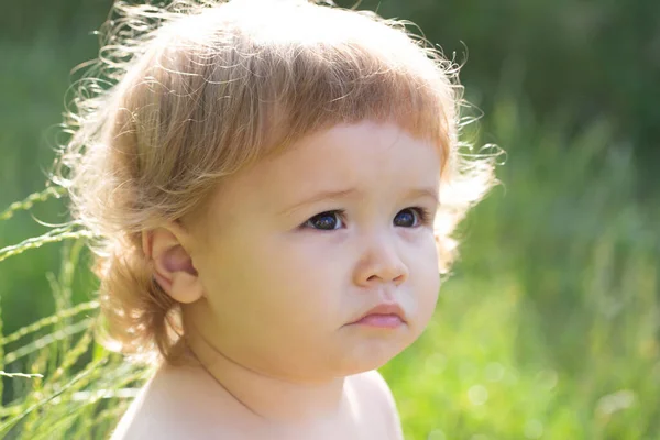 Baby in gras op zonnige zomeravond. Serieus kind buiten. Baby gezicht van dichtbij. Grappig kinderportret. Blond kind, emotie gezicht. — Stockfoto