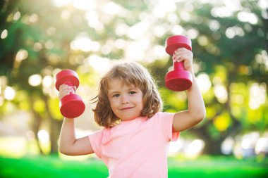 Dambılları açık havada olan yakışıklı sarışın çocuk. Fitness çocukları, sağlık ve enerji. Sağlıklı çocuk yaşam tarzı. Çocuk halterle egzersiz yapıyor. Küçük çocuklar için spor.