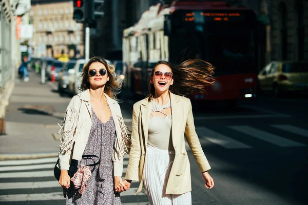 Όμορφα κορίτσια περπατούν στο δρόμο και διασκεδάζουν. Καλύτερες φιλενάδες, στυλ πόλης. Δύο φίλοι γελούσαν και περπατούσαν στο κέντρο της πόλης, φορώντας γυαλιά ηλίου. — Φωτογραφία Αρχείου