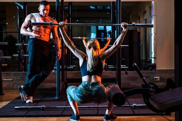 Allenamento femminile con bilanciere in palestra. Allenatore muscolare uomo formazione donna con bilanciere. Personal trainer istruttore di fitness. — Foto Stock