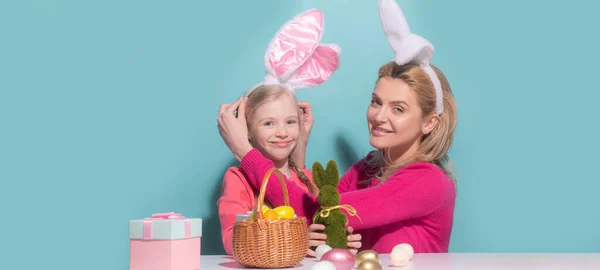 Matka a dcera slaví Velikonoce. Roztomilá holčička s legračním obličejem v králičích uších se směje, usmívá a baví se izolovaně na modré. Velikonoční nápis s kopírovacím prostorem. — Stock fotografie