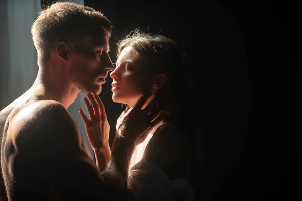 Romantic couple in love looking at each other, embracing and kissing on black background. Beautiful loving couple posing on dark backgroung with night lights. — Stockfoto