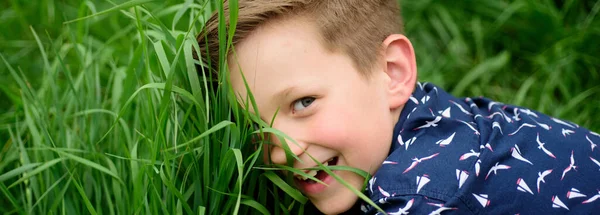 Banner med vårbarns ansikte. Leende pojke med gräs bakgrund. Söt unge som njuter på fältet. Enighet med naturen. Barn på grönt gräs bakgrund. — Stockfoto