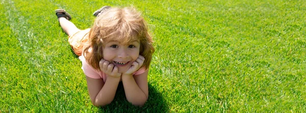 Baner z dziecięcą twarzą. Dzieci leżące w trawie, słodkie dziecko w letnim parku przyrody. Dzieci na zielonym tle trawy. — Zdjęcie stockowe