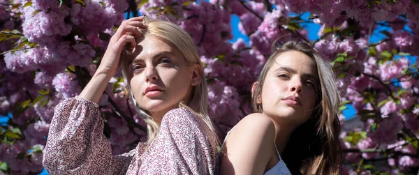 Tavaszi transzparens női barátnőkkel a szabadban. Tavaszi lányok divat. Gyönyörű lány rózsaszín virágokkal a nyári virágos parkban. — Stock Fotó