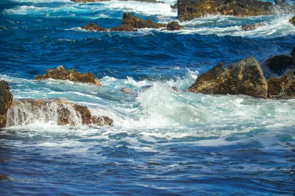 Mořská kamenitá pláž, mořské vlny. Barevné modré moře pozadí. Koncept letní dovolené a cestování. Čistá mořská voda, velké kameny na pláži. — Stock fotografie