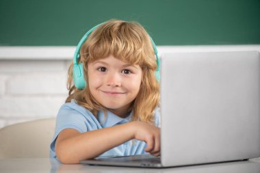 Kulaklıklı zeki çocuk masada oturur, okulda dizüstü bilgisayarda çalışır, klever çocuk internet derslerini kullanarak öğrenirken kulaklık takar. Dahi çocuk programlama.