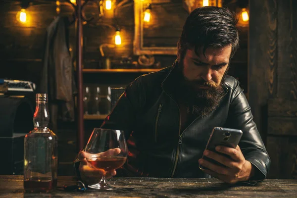 Ciddi, kendinden emin, sakallı, zengin ve cam viskili girişimci. Barda akıllı telefon üzerinde çalışırken viski içen kıdemli bir adam.. — Stok fotoğraf