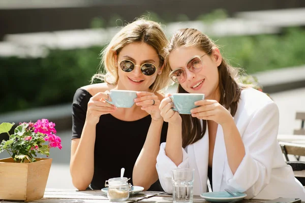 Amigas románticas con taza de café en la cafetería. Pasar un buen rato con el mejor amigo. Dos hermosas mujeres en gafas de sol tomando café al aire libre en la cafetería vintage. Atractivas francesas. — Foto de Stock