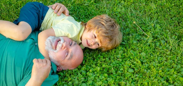 Gelukkige grootvader en kleinzoon ontspannen samen op gras. Kind met grootvader droomt in de zomer in de natuur. Grootvader en kleinkind, voorjaarsspandoek. — Stockfoto