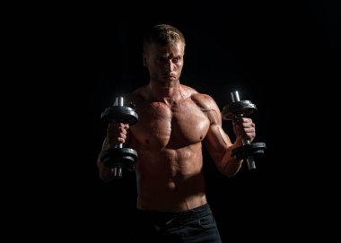 Karanlık stüdyoda dambılla egzersiz yapan genç bir sporcunun portresi. Seksi spor gövdesi, dambılı adam. Crossfit, spor ve sağlıklı yaşam tarzı konsepti.