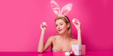 Tavşanlı Paskalya bayrağı. Tavşan kulaklı kadın paskalya yumurtasını pembe arka planda tutuyor..