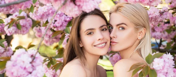 Spring banner with women girlfriends outdoor. Girls in in cherry sakura blossoms flowers. Outdoor closeup portrait of young beautiful sensual fashion girls posing near blooming tree with pink flowers. — Fotografia de Stock