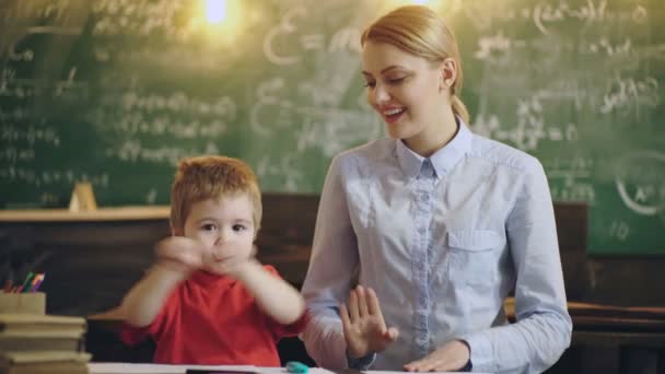 Professora sorrindo ajudando um pequeno aluno na escola primária. — Vídeo de Stock