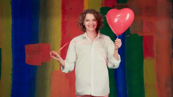 Ładna kobieta wysyła pocałunek powietrza z czerwonym balonem kształt serca na tle koloru. Świętowanie i gratulacje. Świętowanie Walentynek. — Wideo stockowe